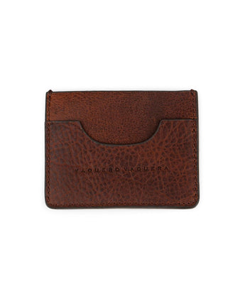 El Tarjetero De Res by VAQUERO VAQUERA es un tarjetero de piel marrón con grano visible, bordes cosidos, logotipo de la marca en relieve y una única ranura para tarjetas, que se muestra sobre un fondo blanco.