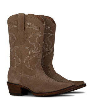 La Santa María - Bota de Gamuza Shell de VAQUERO VAQUERA cuenta con ante color canela, costuras blancas, tiras, puntera en punta y tacón de madera apilado. Estas botas para mujer se muestran con estilo una al lado de la otra, ligeramente inclinadas hacia la derecha.