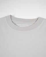 Primer plano de una camiseta Gris claro Tee de VAQUERO VAQUERA, unisex de cuello redondo en gris claro, tumbada y mostrando el cuello y la etiqueta interior de tamaño medio.