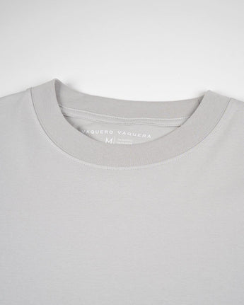 Primer plano de una camiseta Gris claro Tee de VAQUERO VAQUERA, unisex de cuello redondo en gris claro, tumbada y mostrando el cuello y la etiqueta interior de tamaño medio.