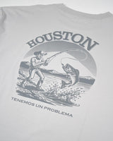 La Houston Tee de VAQUERO VAQUERA es una playera gris unisex con ilustración western de vaquero pescando, montañas y texto: HOUSTON arriba y TENEMOS UN PROBLEMA abajo.