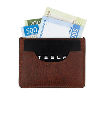 Un tarjetero de res VAQUERO VAQUERA de diseño minimalista sostiene una tarjeta negra con el logo de Tesla y varios billetes mexicanos, incluidos dos de $500 y uno de $200, que se asoman parcialmente.