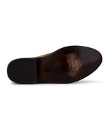 La imagen muestra la suela de un Alamo Bota de Gamuza Bentley marrón oscuro de VAQUERO VAQUERA, con la parte inferior de piel ligeramente desgastada, el nombre y el logotipo de la marca cerca del arco y un tacón con tachuelas redondas de agarre que recuerdan a las botas vaqueras clásicas.