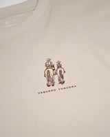 La familia Tee de VAQUERO VAQUERA: playera beige con diseño western de dos personas a caballo vistas de espaldas, sobre las palabras "VAQUERO VAQUERA".