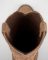 Vista de arriba abajo de la apertura de un Alamo Bota de Gamuza Bentley color canela de VAQUERO VAQUERA, con "VAQUERO" impreso en el forro interior oscuro. El fondo es de color claro y está desenfocado.