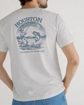 Una persona lleva una camiseta Houston Tee de VAQUERO VAQUERA de color gris claro con un pescador capturando un gran pez en la espalda, con "HOUSTON" encima, "TENEMOS UN PROBLEMA" debajo y un elegante toque western.