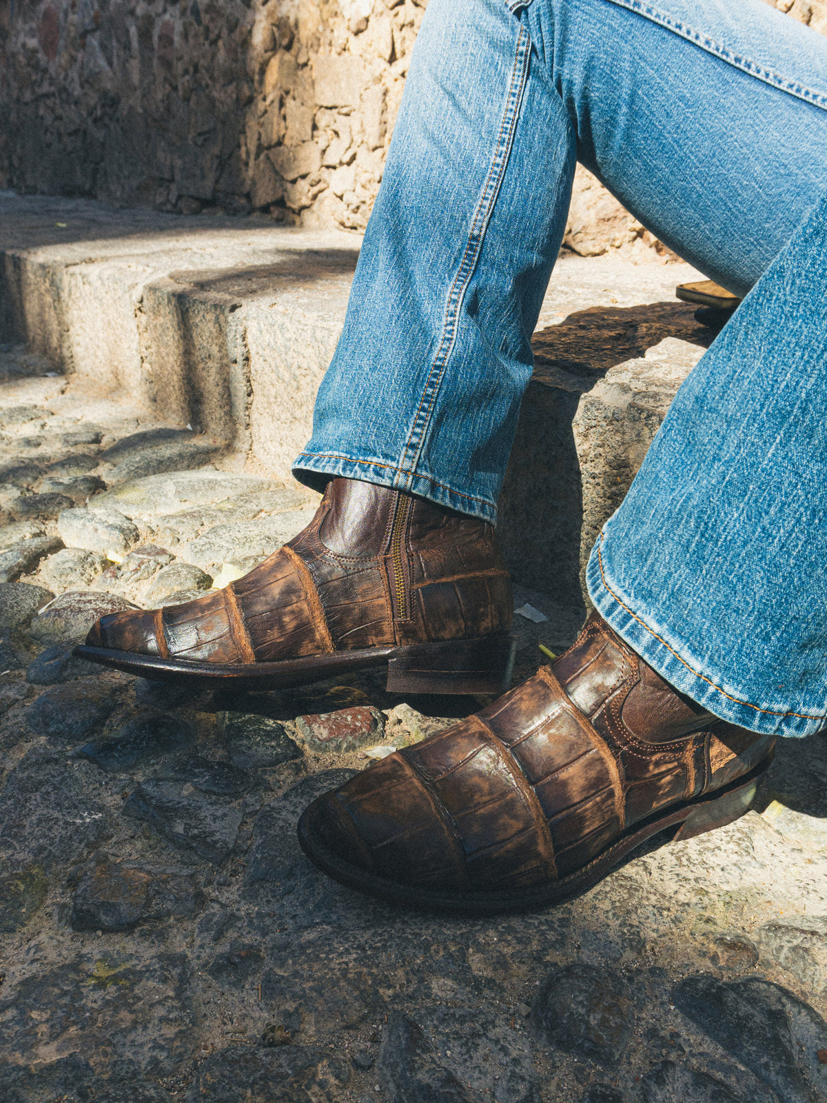 Botas de piel café con jeans sobre escalones de piedra.