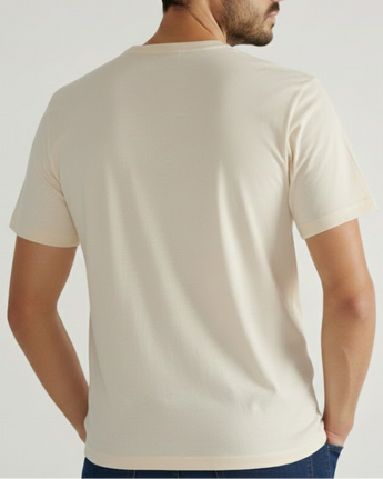 Un hombre de espaldas a la cámara viste la camiseta VAQUERO VAQUERA Beige Tee y pantalones oscuros sobre un fondo claro.